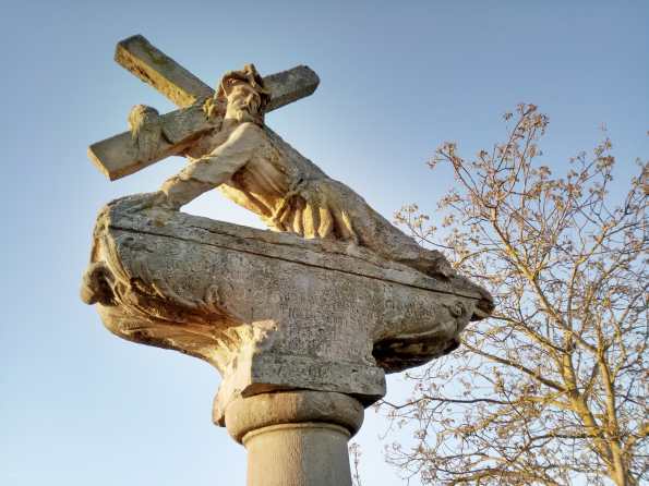 Jesus mit dem Kreuz als Steinfigur am Wegesrand