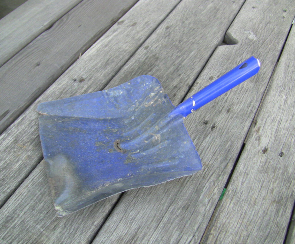 eine alte blaue Kehrschaufel liegt auf altem Holz